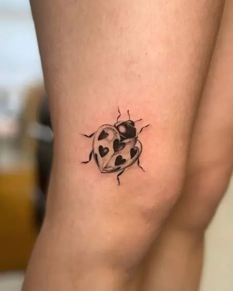 a ladybug tattoo on the leg with black dots and hearts in it's center