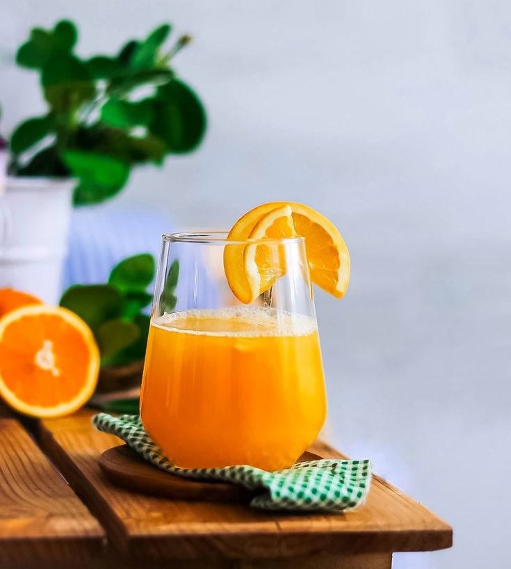 a glass filled with orange juice sitting on top of a wooden table next to an orange slice