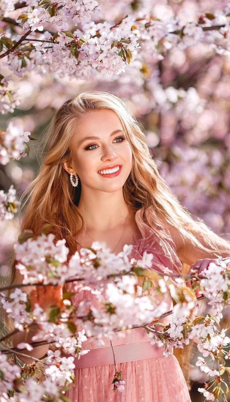 a beautiful blonde woman standing in front of pink flowers