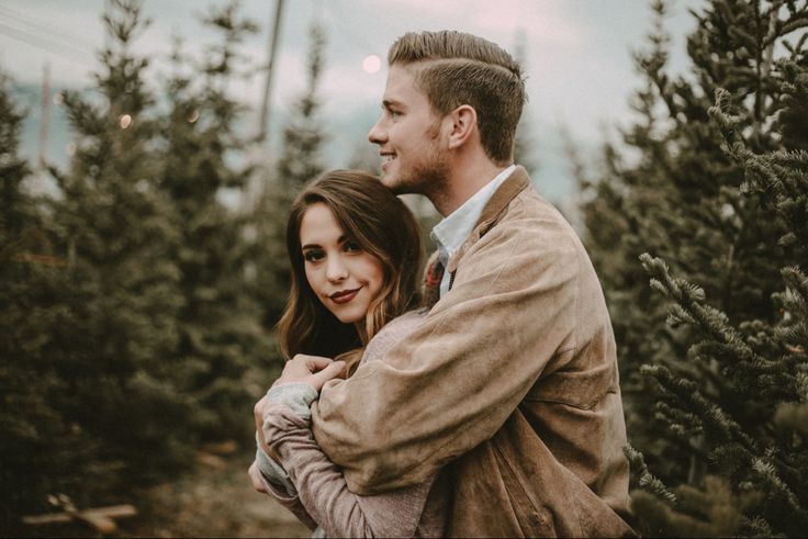 a man and woman hugging in front of christmas trees at an outdoor tree farm during the day