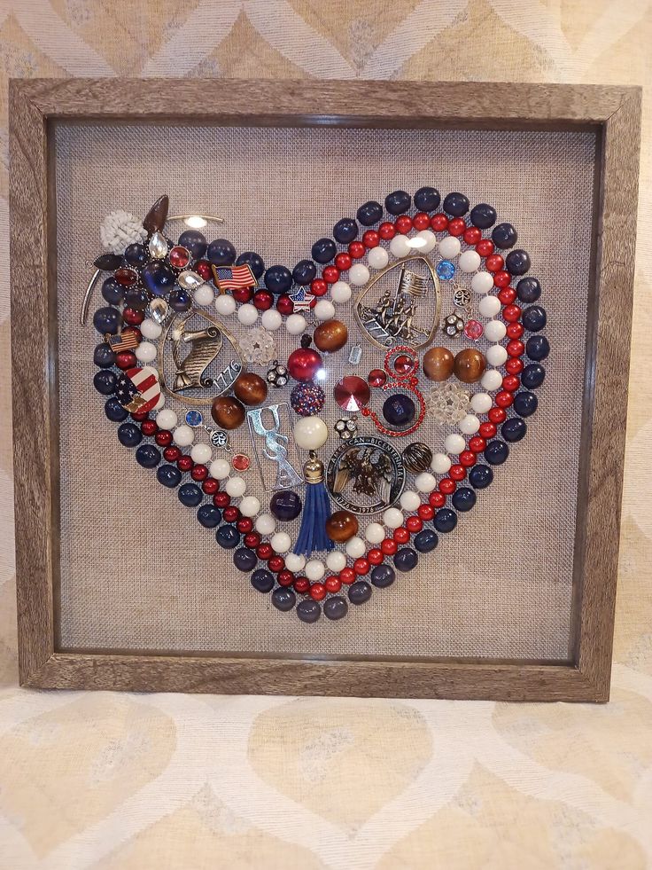 a heart made out of beads and other items in a frame on a wall or floor