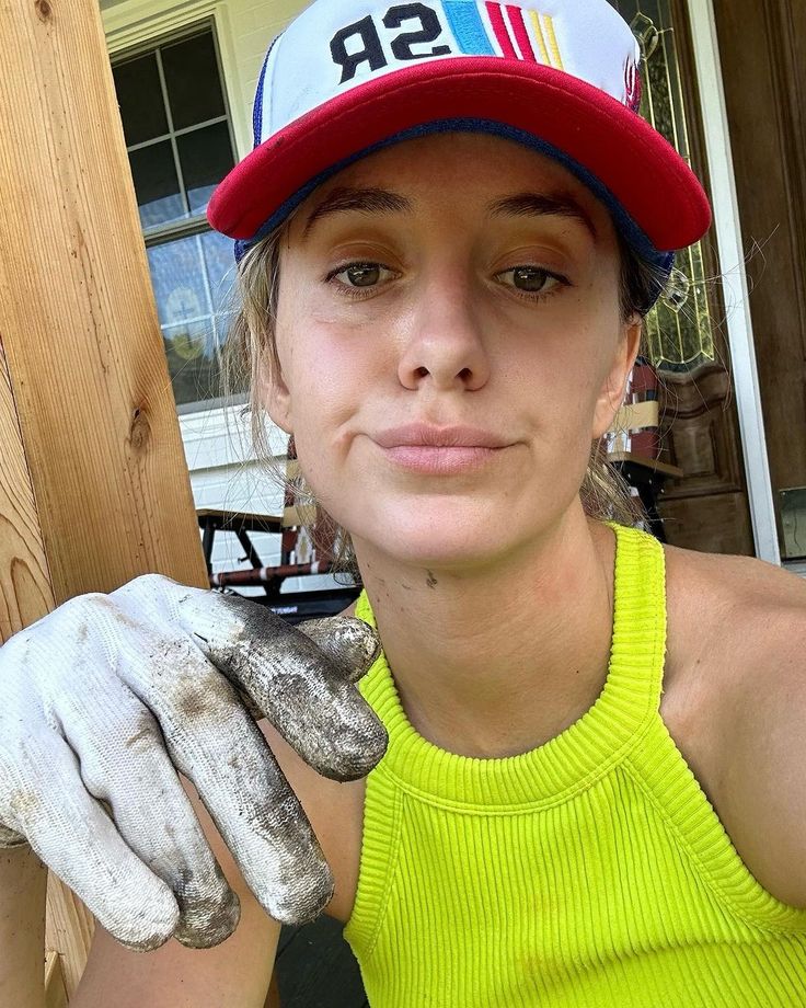 a woman in a yellow shirt and red hat is holding some white gloves on her left hand