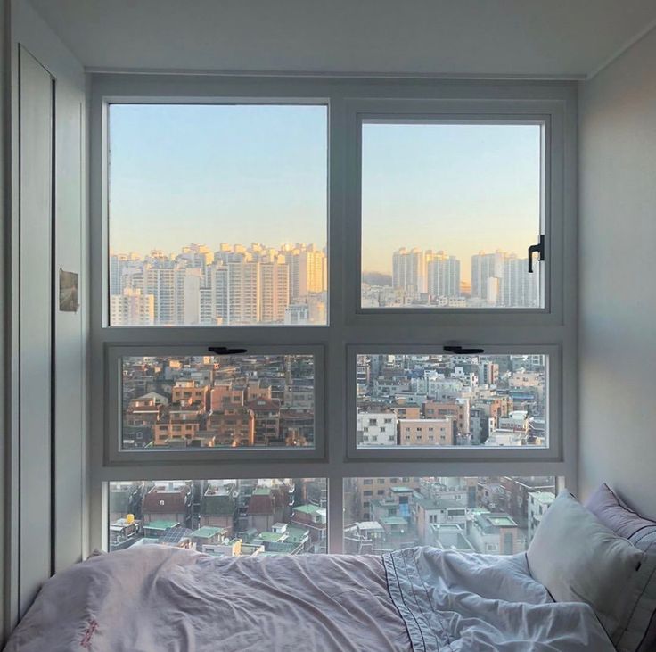 a bed sitting in front of two windows next to a window sill with city view