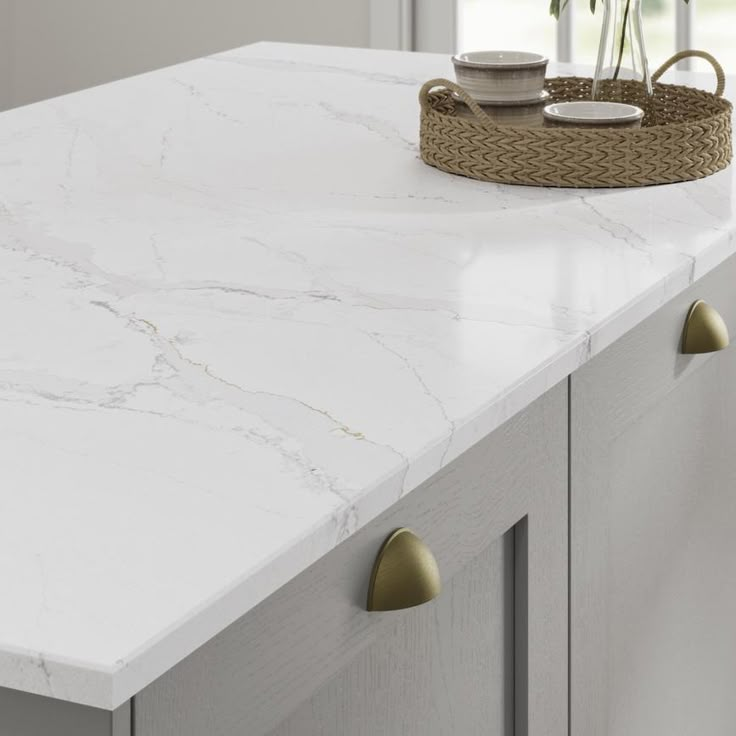 a white counter top with brass handles and some plants on it in a basket next to the counter