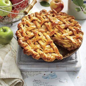 an apple pie with one slice cut out and apples in the background on a table