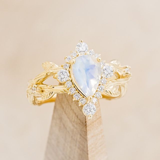 a yellow gold ring with a pear shaped blue and white stone surrounded by small diamonds