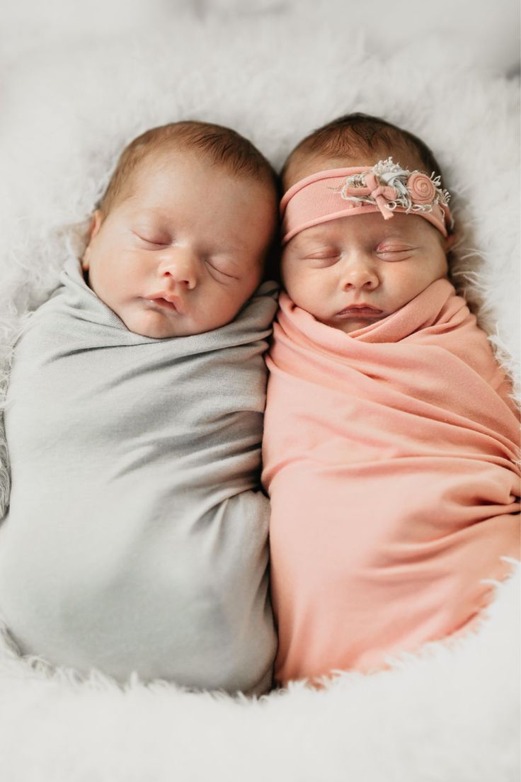 two newborn babies wrapped in blankets sleeping on a white furnishing blanket with their eyes closed