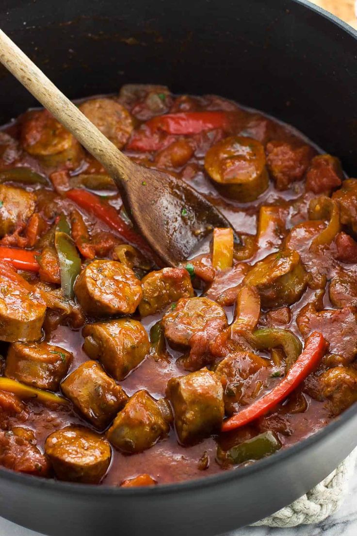 sausage and peppers in a skillet with a wooden spoon