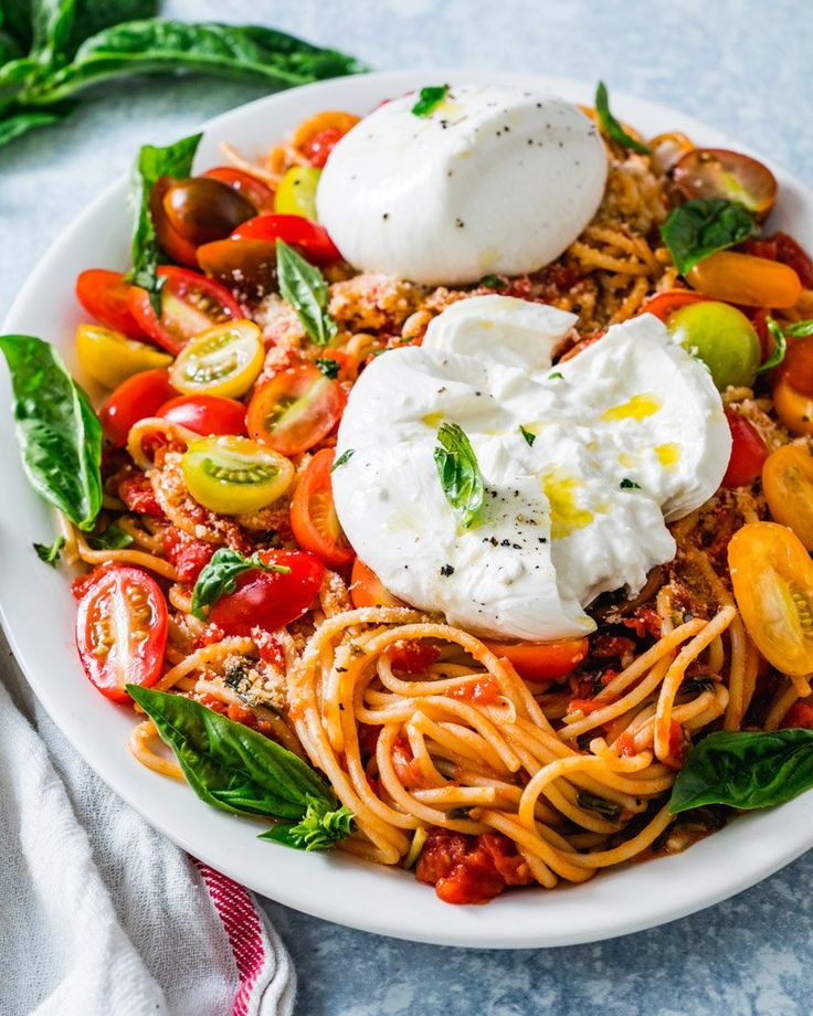 a white plate topped with pasta, tomatoes and mozzarella on top of a blue table cloth