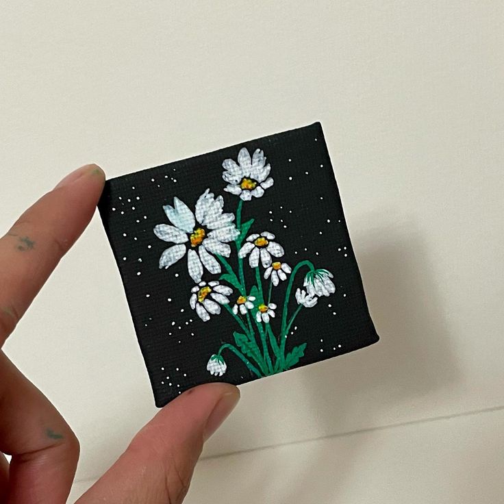 a hand holding up a piece of black and white paper with daisies on it