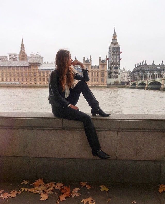 a woman sitting on the edge of a wall next to a body of water with buildings in the background