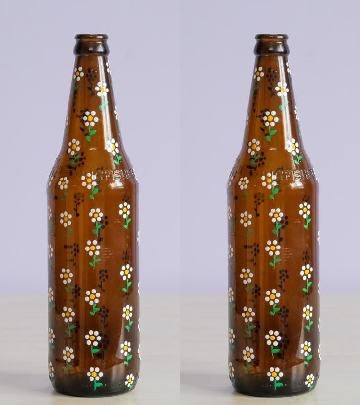 two brown beer bottles with white flowers painted on the top and bottom one is empty