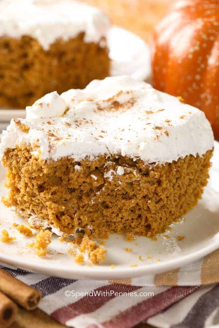 a slice of pumpkin cake on a plate with whipped cream frosting and cinnamon sticks