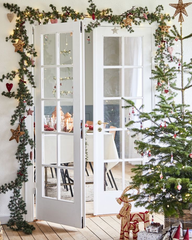 a decorated christmas tree sitting in front of a white door with two glass doors open