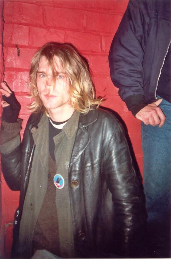 a man in a leather jacket standing next to a brick wall