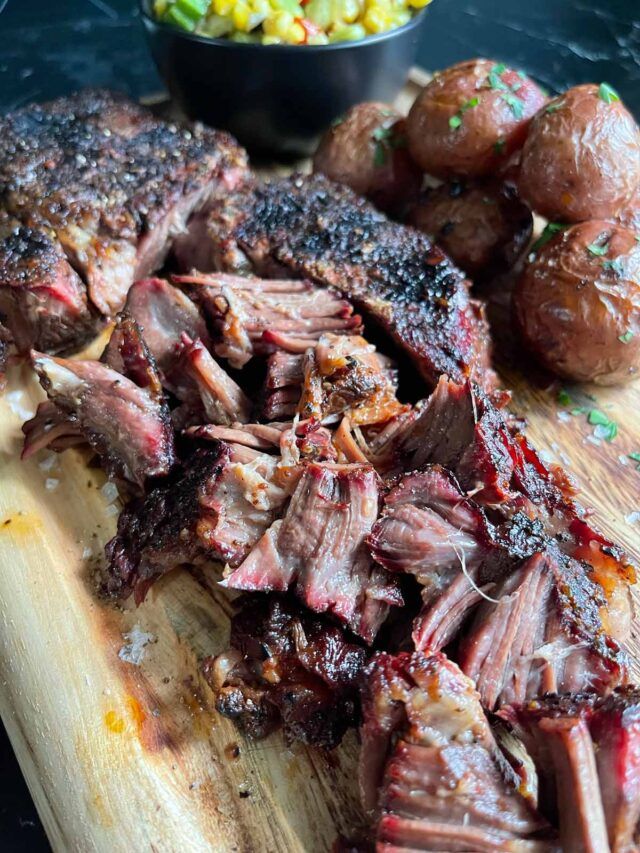 steak and potatoes on a cutting board next to a bowl of corn kernels in the background