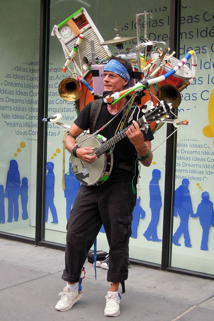 a man is walking down the street with a guitar and musical instrument on his head