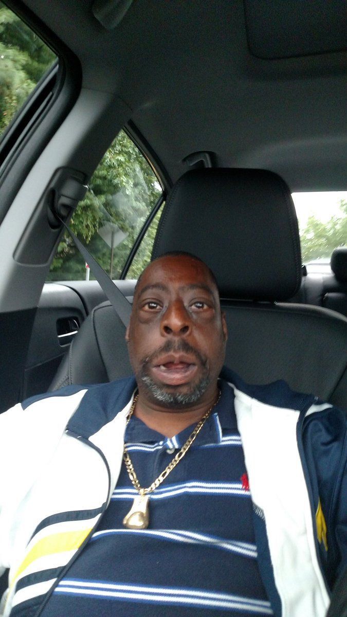 a man sitting in the back seat of a car wearing a striped shirt and necklace