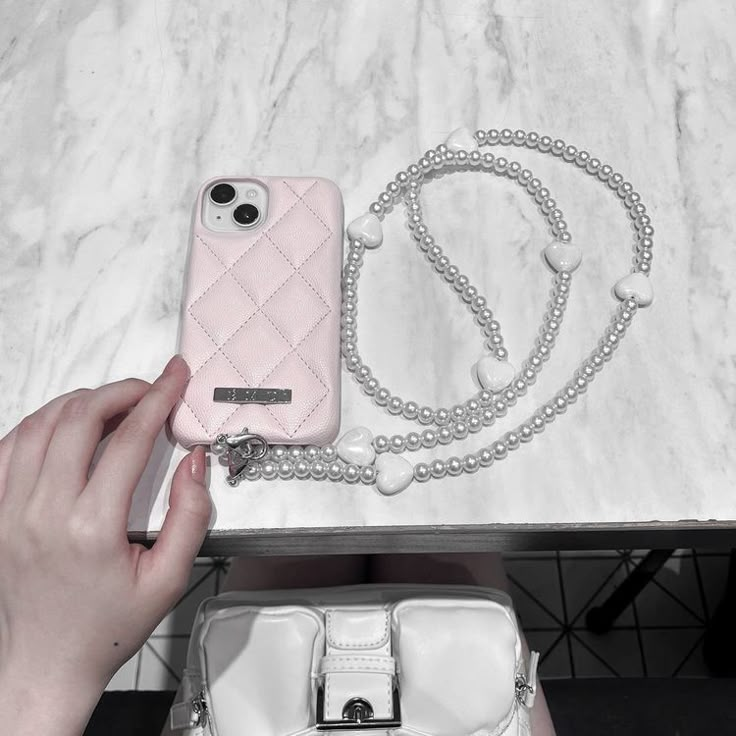 a person holding a cell phone next to a white purse on top of a table