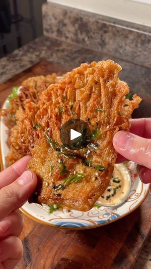 someone is holding up some fried food on a white and blue plate with green olives