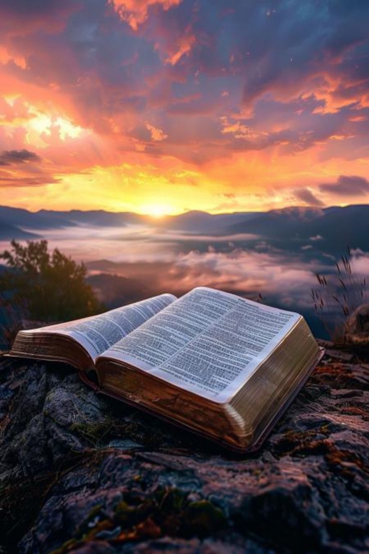 an open book sitting on top of a rocky cliff under a cloudy sky at sunset