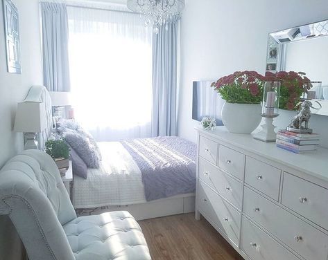 a bedroom with white furniture and flowers in the window sill, along with a large mirror