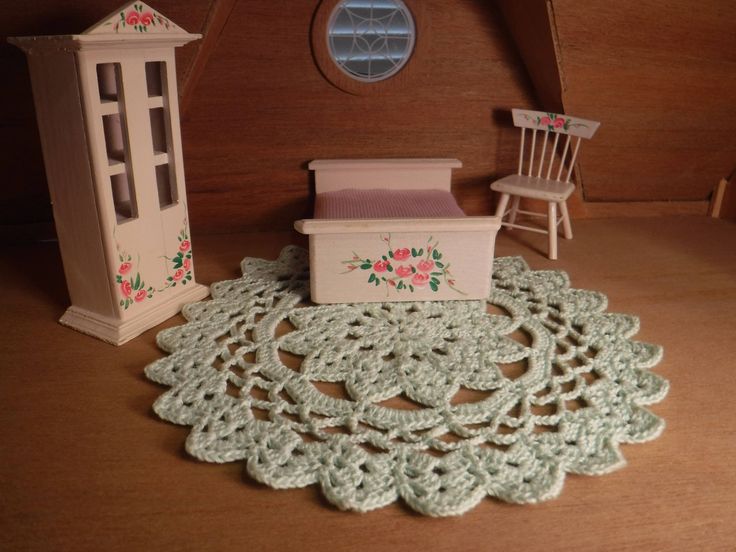 a doll house with furniture and crocheted doily on the floor in front of it