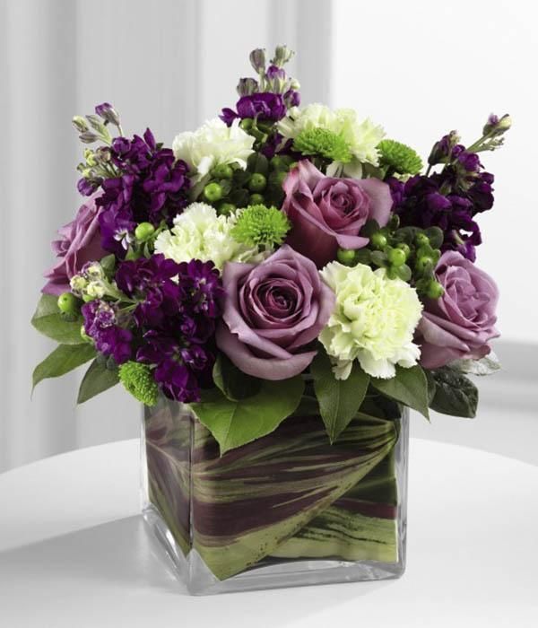 a square vase filled with purple and white flowers