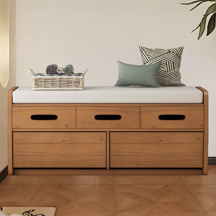 a wooden bench with two drawers and a pillow on top of it next to a potted plant