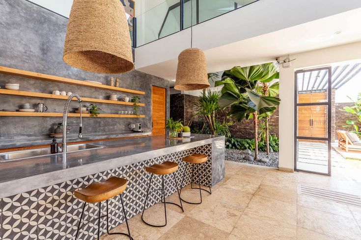 a kitchen with an island counter and stools in front of the bar area that has plants on it