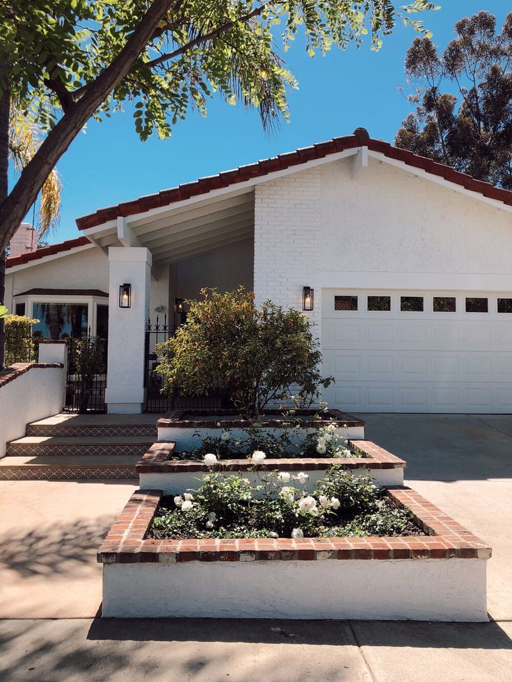 a white house with red roof and brick planters