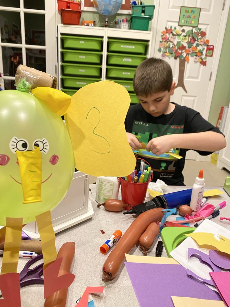 a young boy is working on crafts with balloons and other crafting supplies in the background