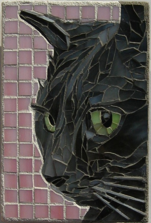 a close up of a black cat with green eyes on a mosaic tile wall background