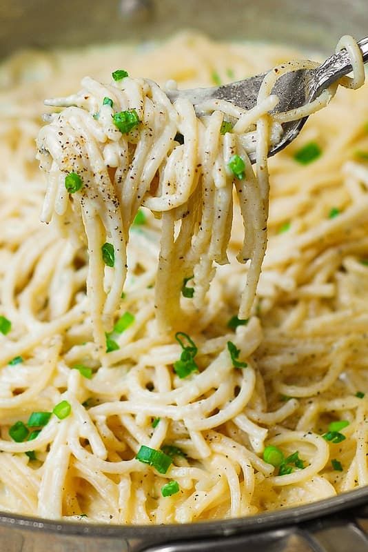 a fork full of pasta with peas and parmesan cheese on it in a skillet