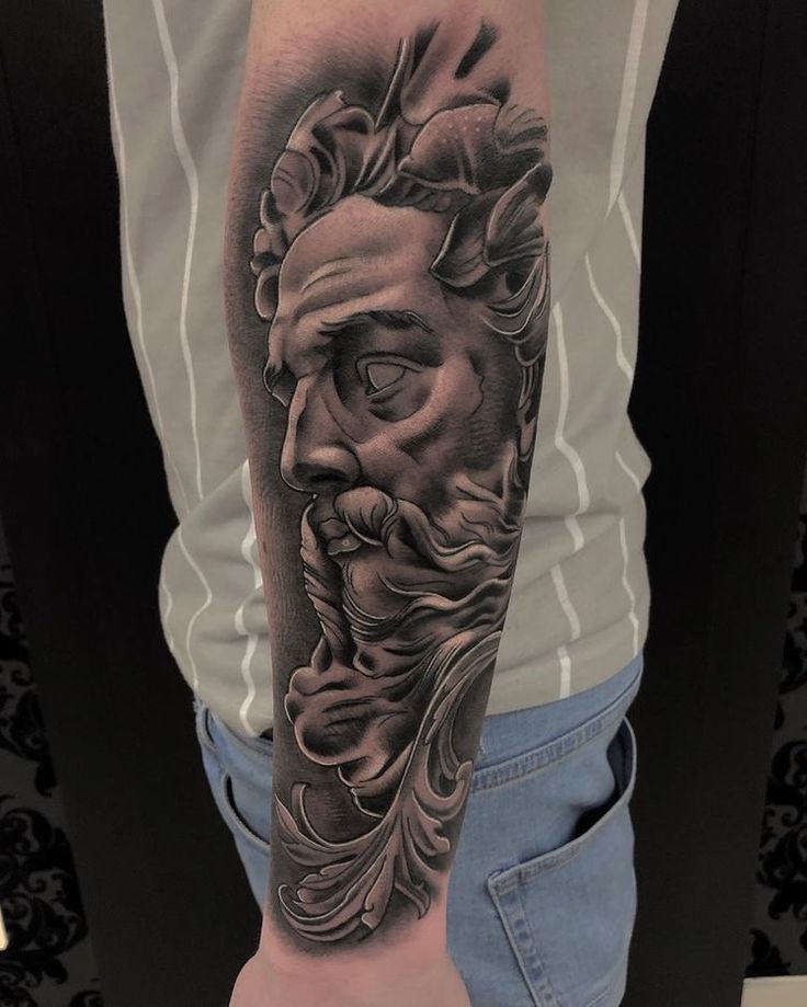 a man's arm with a black and grey tattoo on it, depicting the face of an ancient greek god