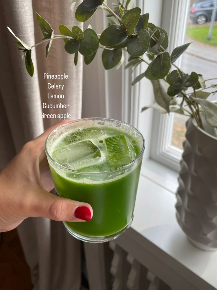 a hand holding a green drink in front of a window