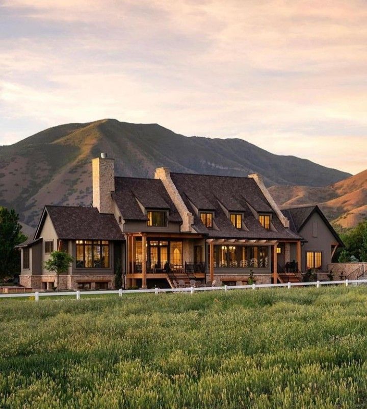 an image of a large house in the middle of a field with mountains in the background