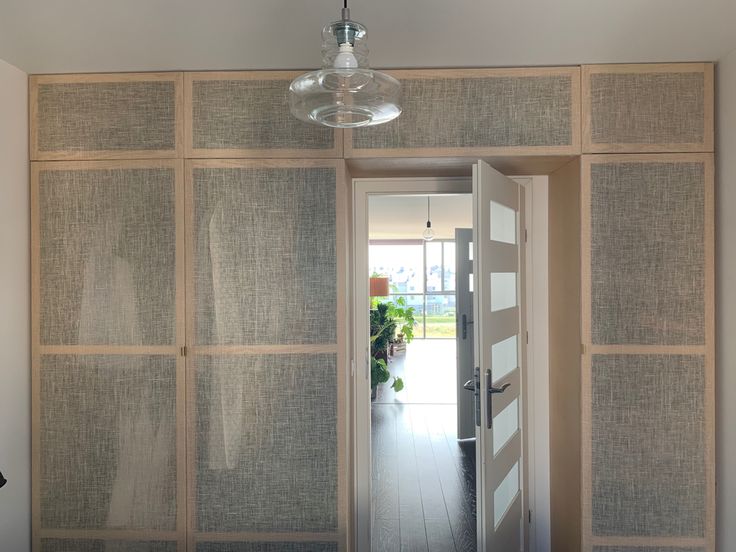 an open door leading to a hallway with wall coverings on both sides and a light fixture hanging from the ceiling