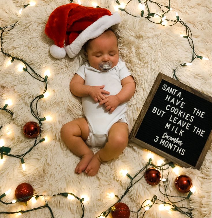 a newborn baby wearing a santa hat and sleeping next to a sign that says santa have cookies but leave the milk for 3 months