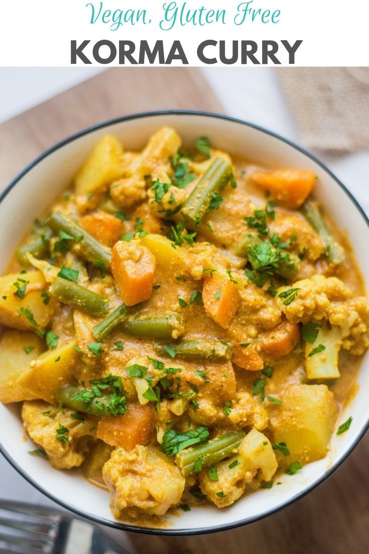 a white bowl filled with curry and vegetables on top of a wooden table next to a fork