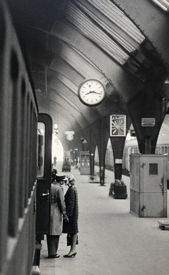 people are standing on the platform waiting for their train to arrive at the station in black and white