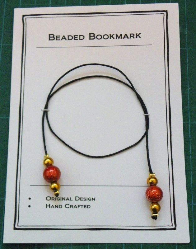 the beaded bookmark has two red beads on black cord with gold balls attached to it