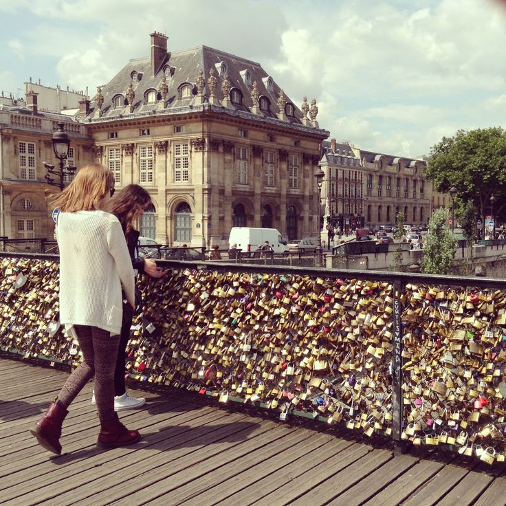 a woman is looking at her cell phone on the bridge covered in padlocks