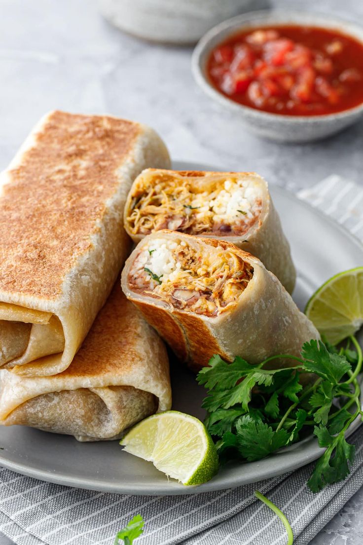 two burritos cut in half on a plate with salsa and cilantro