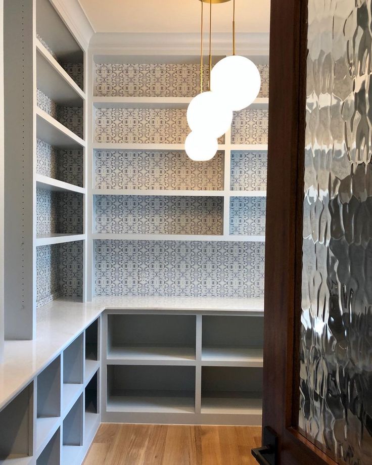 an empty room with white shelves and silver tiles on the walls, along with a wooden floor