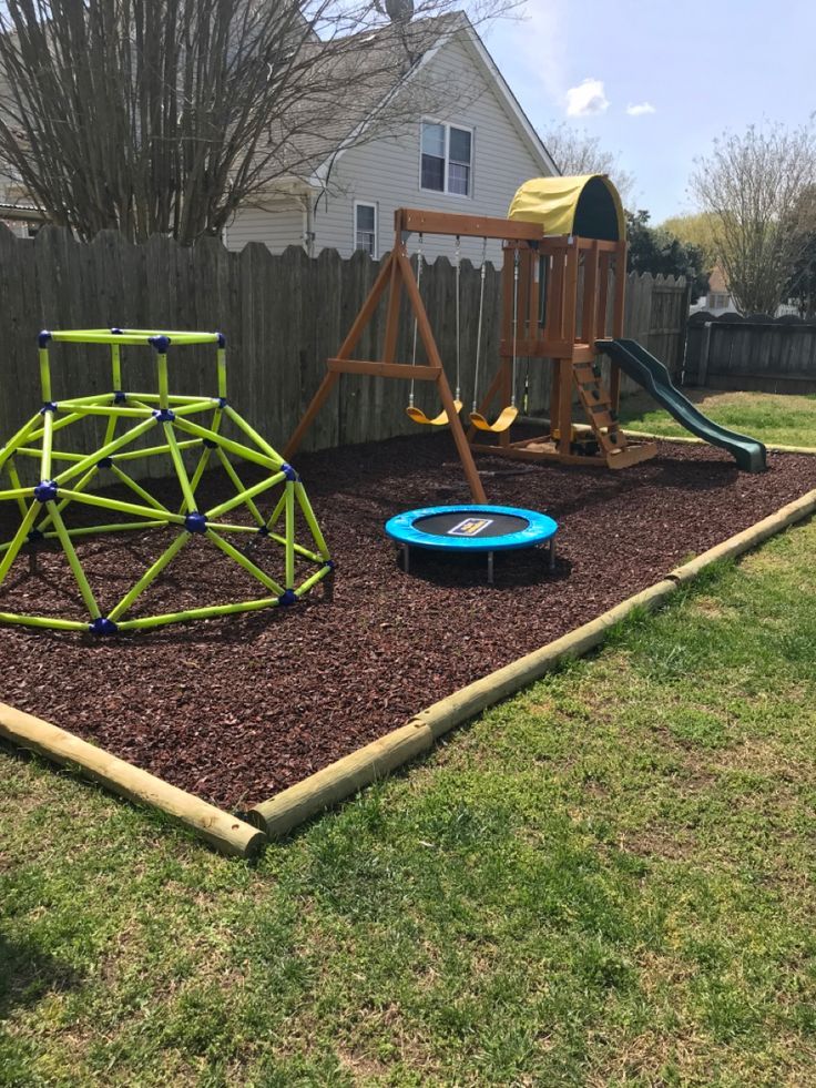 a backyard play area with a swing set, slide and climbing frame in mulch