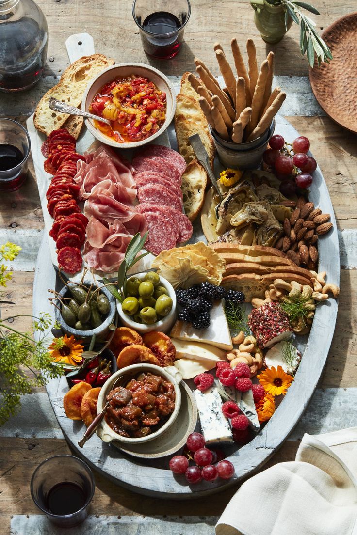 a platter filled with meats, cheeses and other foods next to glasses of wine