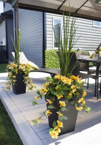 two large planters with yellow flowers are on the back porch near a table and chairs