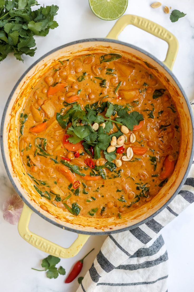 a large pot filled with soup and garnished with cilantro, green onions, carrots and peanuts