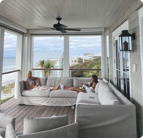 two women sitting on couches in front of large windows overlooking the ocean and beach